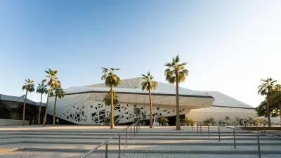 exterior view of an angular modern building with palm trees in front and a staircase in the foreground