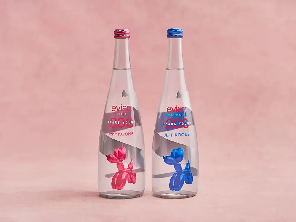 two clear glass bottles in front of a light pink backdrop. The one on the left has an image of a pink balloon dog on the label, and the one on the right has a blue balloon dog.