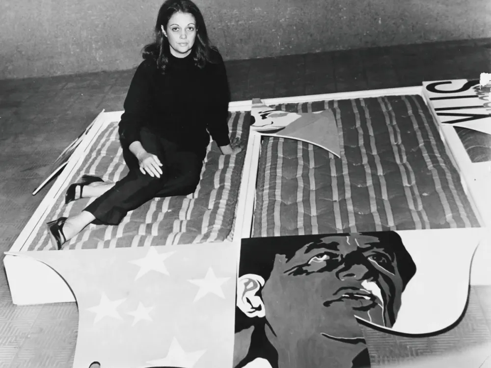 An archival image of a woman seated on an artwork made of three mattresses.