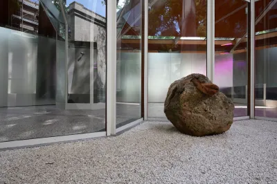 A large rock sits outside a glass structure. 