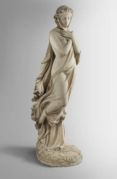 A sculpture of a nude woman holding a veil to her face and walking forward.
