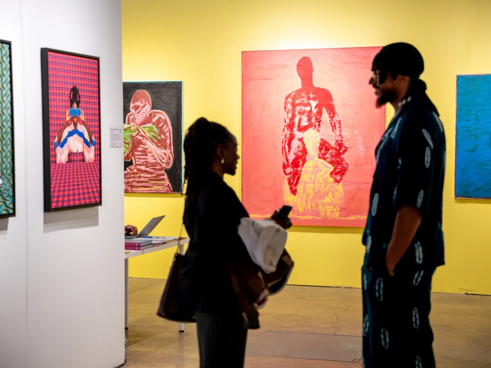 Two figures standing in the midst of colorful paintings.