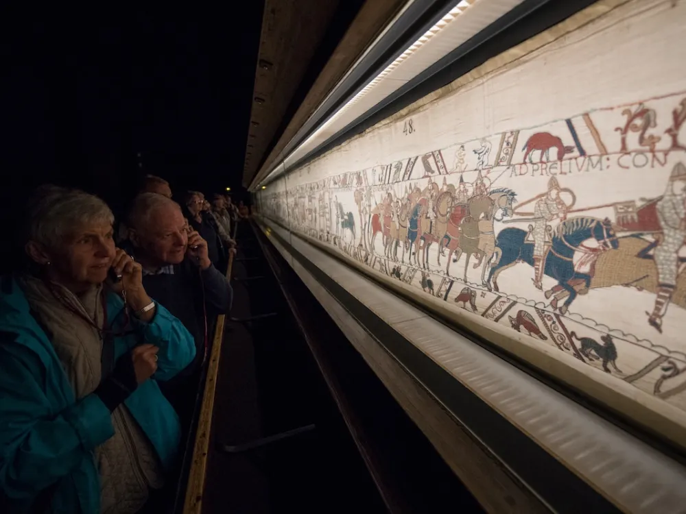 People looking at a tapestry showing people on horseback.