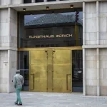 A man walks past gold double doors.