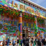A group of people walking in front of a colorful, columned building with the words 