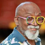 close up of a bald man with a white beard and mustache and colorful eyeglass frames