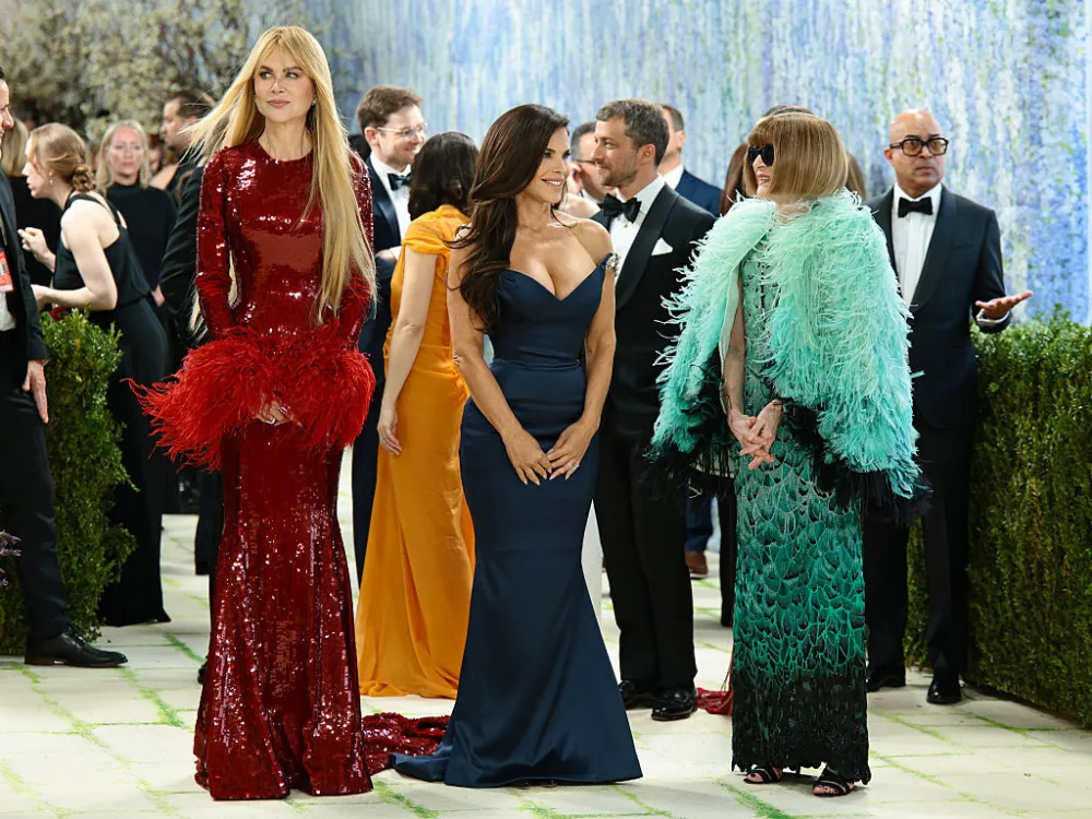 A group of three women, on the left a red sequined dress, in the middle a low-cut sleeveless dark blue dress, on the right a black and turquoise dress with a feathery shawl