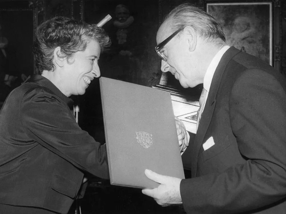 A photo shows Hans H. Biermann-Ratjen, wearing a suit, presenting an award to Hannah Arendt.