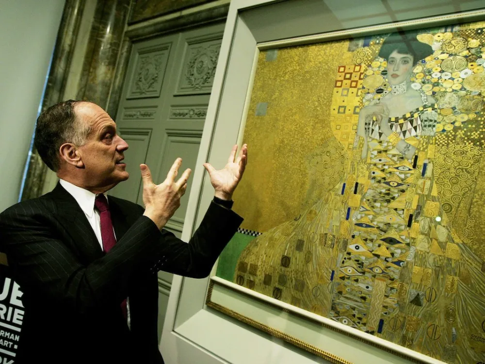 A man raising his arms before a painting of a woman in a golden dress.