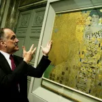 A man raising his arms before a painting of a woman in a golden dress.