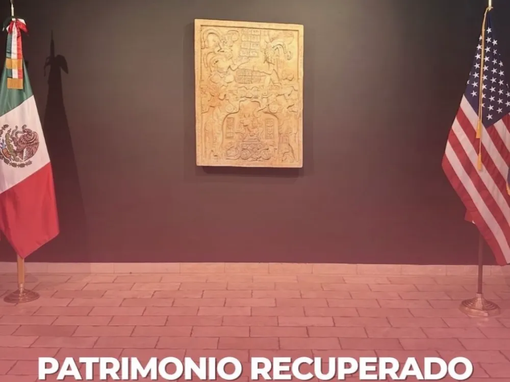 a room with a carved stone object on the wall and a Mexican flag on the left and American flag on the right