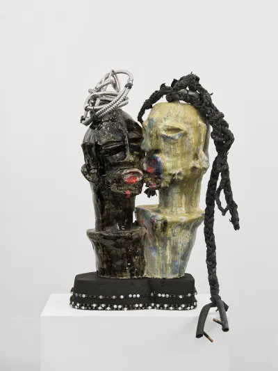 A sculpture of two heads, one of which appears to be kissing the other. Both are adorned with tangles of trash.