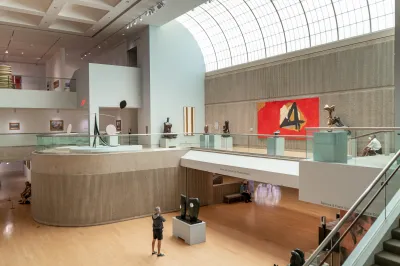 A photo shows a high-ceilinged art museum gallery with numerous modern artworks on display and skylights bringing in daylight