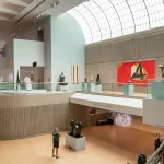 A photo shows a high-ceilinged art museum gallery with numerous modern artworks on display and skylights bringing in daylight