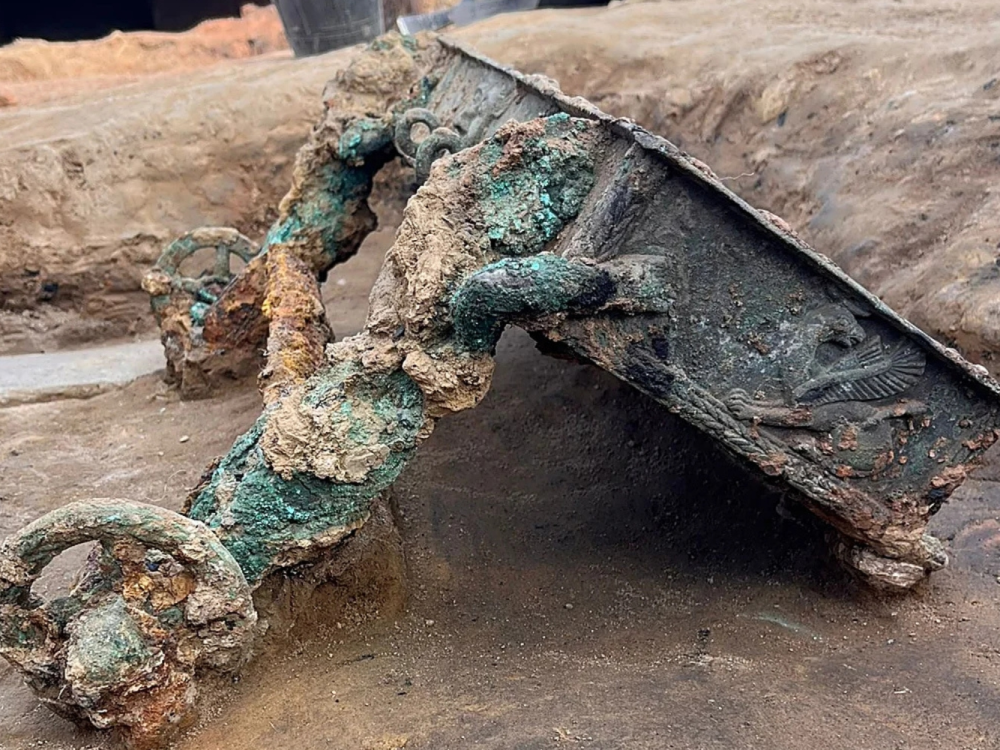 A photo shows a large fragment of a bronze chariot unearthed at an archaeological site.