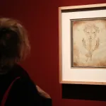 A woman looks at a paiting in a frame hung on a red wall.