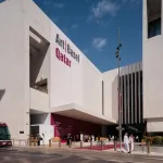 A modern looking sand colored building with the words Art Basel Qatar written on the left.