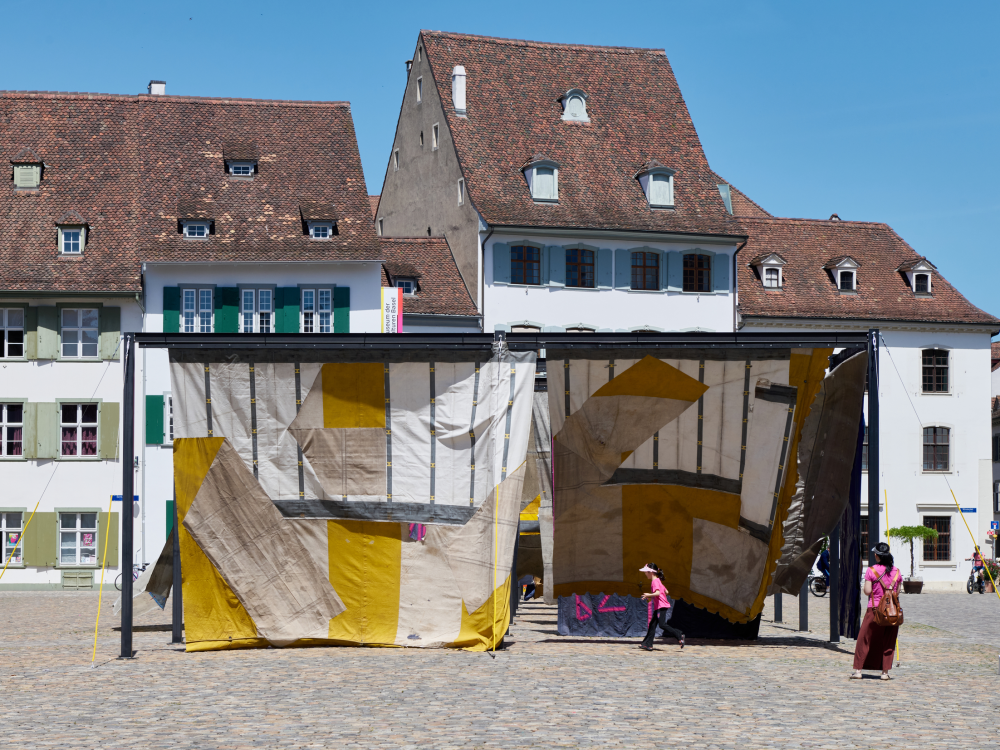 View of an installation made of stitched together textiles and other materials in a Swiss plaza.