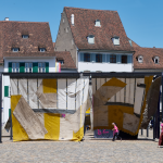 View of an installation made of stitched together textiles and other materials in a Swiss plaza.