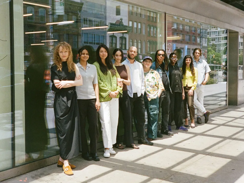 A group of people stand in a single file alongside a wall of windows on the exterior of a building.
