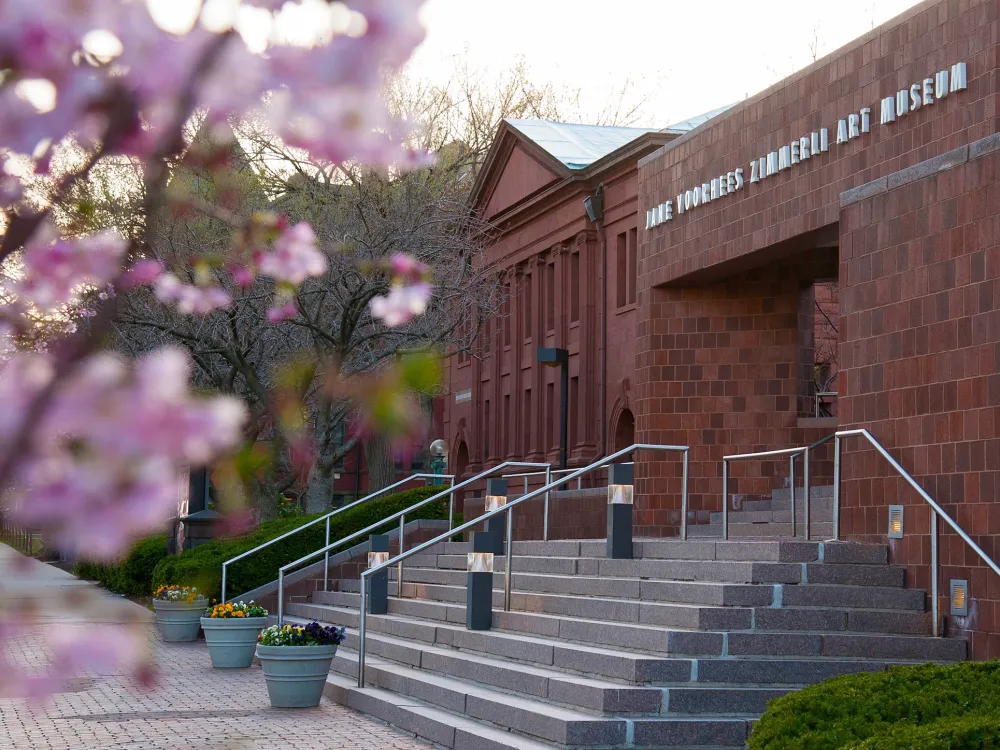 A photo shows a brick building with a nameplate reading The Jane Voorhees Zimmerli Art Museum. A flowering tree blooms in the foreground.