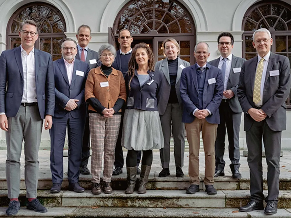 A group of ten people mostly in business attire pose smiling for the camera on the steps in front of a building.
