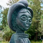 An outdoor metal statue shows a stylized, geometric face.