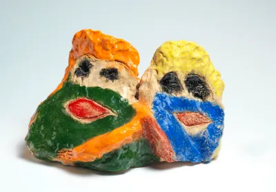 A brightly painted ceramic artwork seems to show two lumpy human figures, head and shoulders, side by side