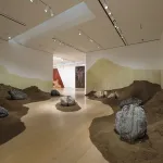 View of a museum with a mounds of soil lining the walls creating a path to the next gallery.