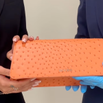 Two set of hands hold an orange handbag.