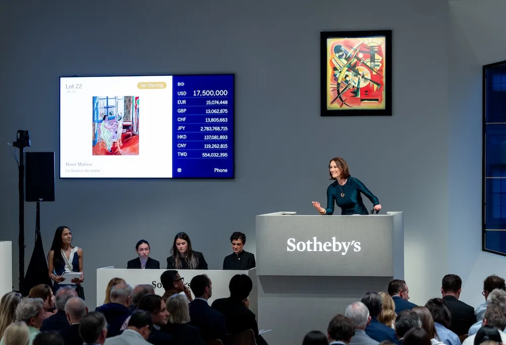 A dark haired woman behind a rostrum emblazoned with the name "Sotheby