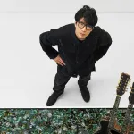 A man in glasses staring upward next to two guitars.
