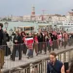 a group of people walking across a bride holding red flags and banners