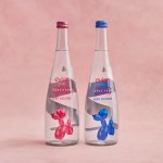 two clear glass bottles in front of a light pink backdrop. The one on the left has an image of a pink balloon dog on the label, and the one on the right has a blue balloon dog.