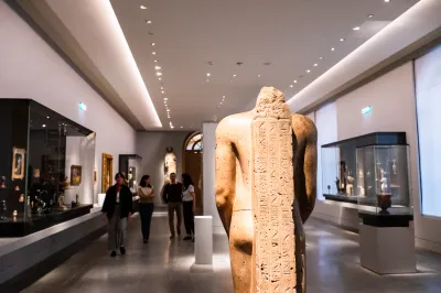 People walk through a museum gallery with an ancient Egyptian sculpture in the foreground.