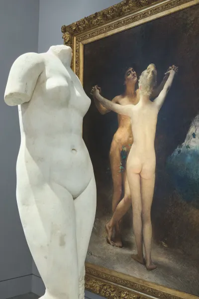 A marble sculpture in front of a painting of two nude women.