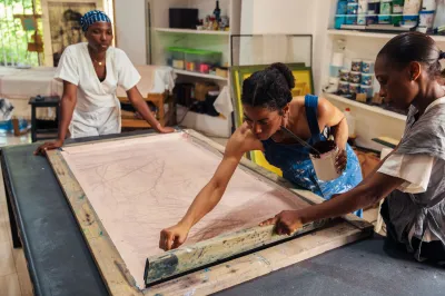 A woman works on a screenprint with two assistants look on.
