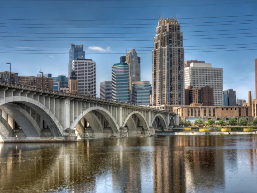 Large buildings reach toward a blue sky in city of Minneapolis behind a peaceful view of St. Anthony Falls.