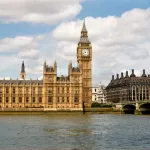 A group of buildings and a clocktower next to a river.