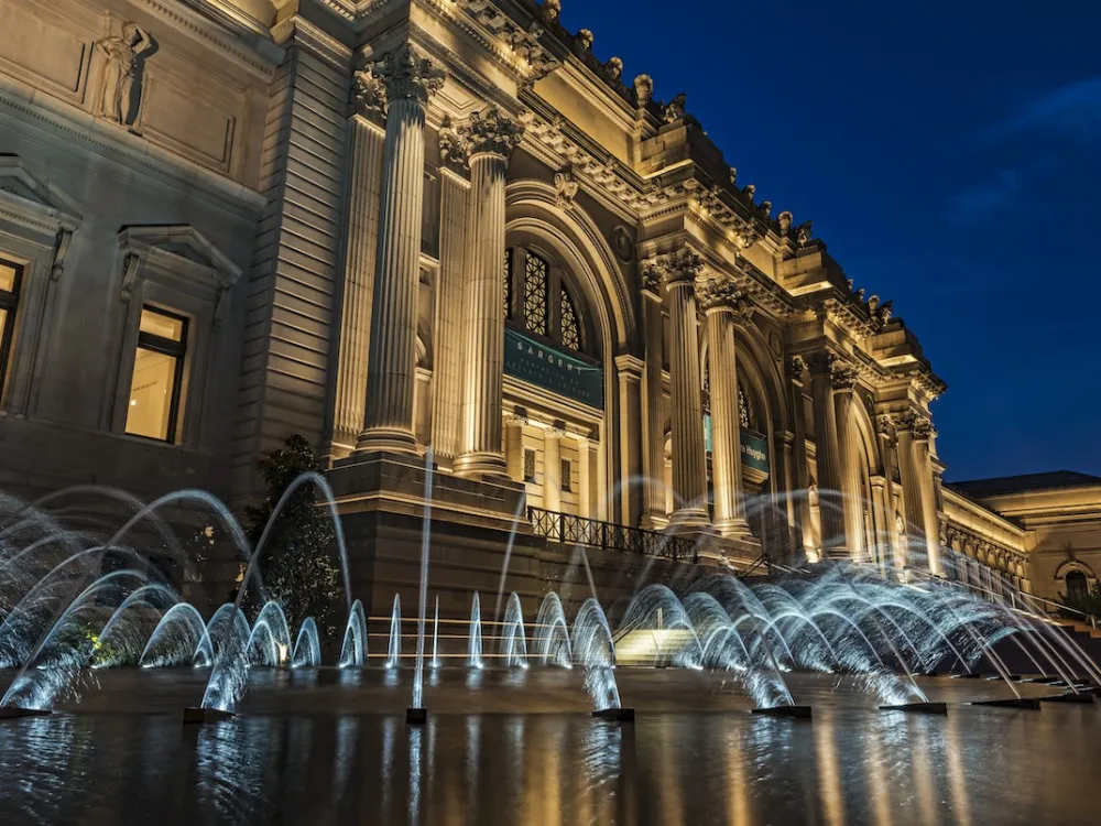 A lit-up building at twilight with a fountain in front of it.