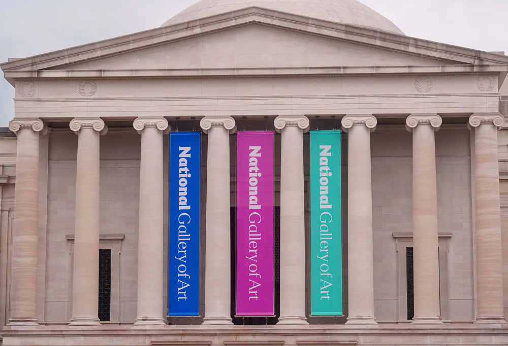 exterior of a columned marble building with blue, pink, and teal banners hanging between columns that say