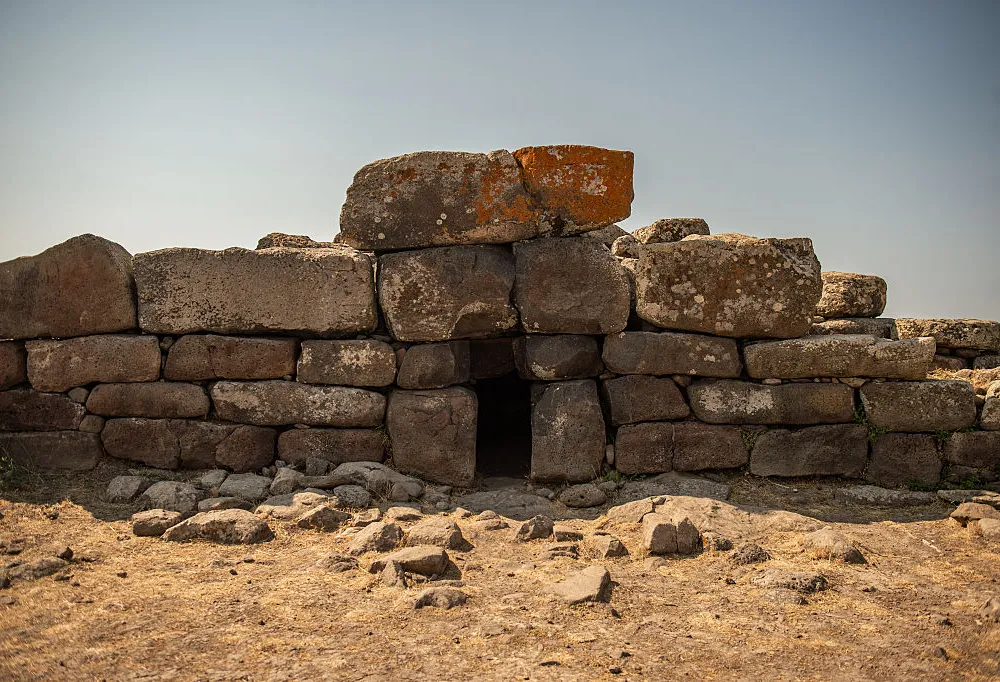 a stone structure with a central opening set amid a dirt ground