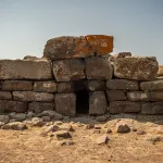a stone structure with a central opening set amid a dirt ground