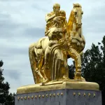 close-up of a gold statue showing a male figure astride a horse with a female figure standing next to it