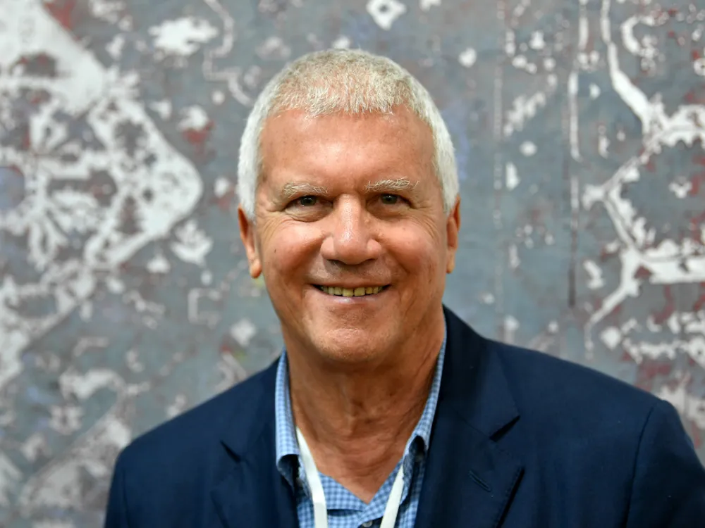 A smiling man wearing a suit in front of an abstract painting.