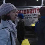 Protesters walk a picket line near a large sign reading Solidarity