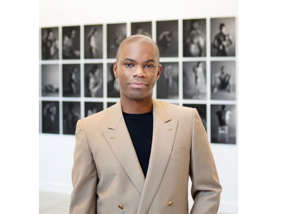 A handsome Black man in a black shirt and tan double-breasted blazer.