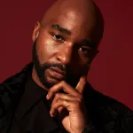 A man looks at the camera against a red background