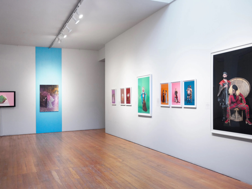 A photograph shows an art gallery with several large colorful photographs hanging on the wall.