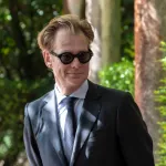 A smiling blond white man, museum director Philippe Vergne, wears a suit and tie and sunglasses.